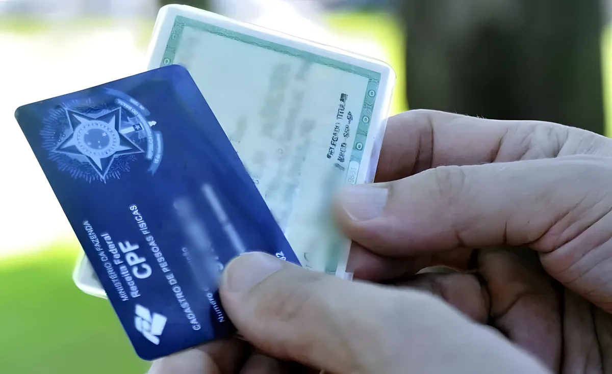 Mão segurando cartão do CPF e carteira de identidade